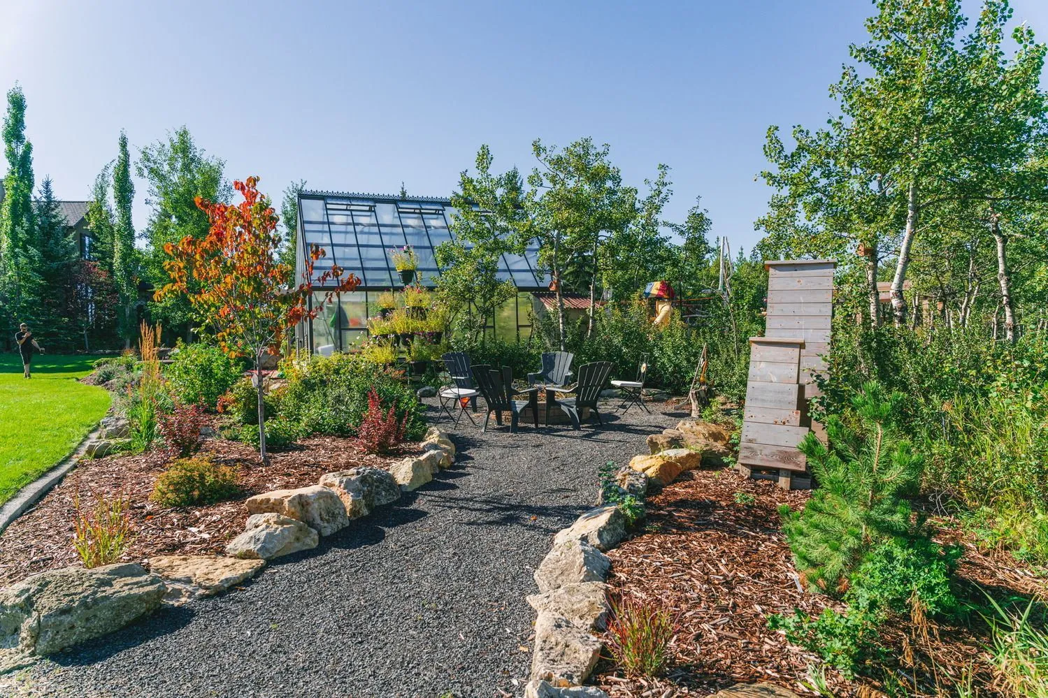 landscaped backyard with gravel path, seating area and greenhouse
